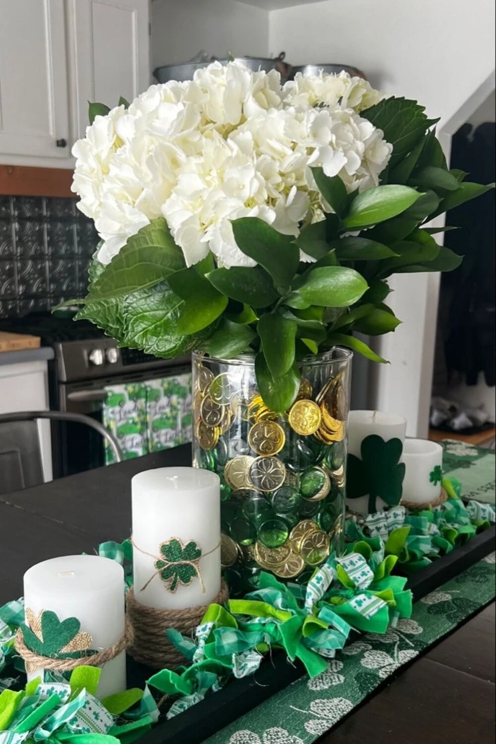 a table with green plant white flower in vase and white candles for saint patrick day